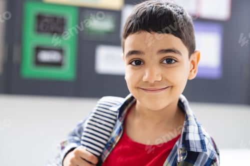Preview: In school, young biracial boy with a striped backpack is smiling in the classroom