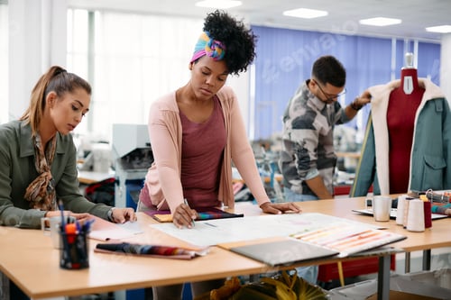 Preview: Black fashion designer and her coworkers working on new sketches at clothing studio.