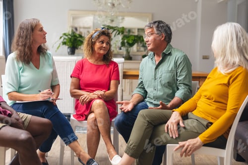 Preview: Caucasian senior man discussing with multiracial people during group therapy session