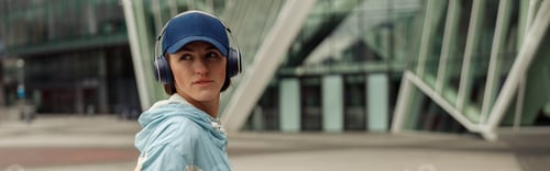 Preview: Sportive woman in headphones stands with bottle of water after running in city. Healthy lifestyle