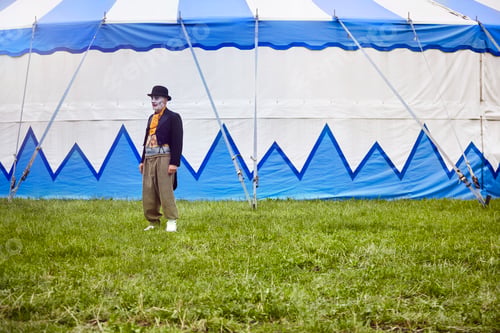 Preview: An old man stands alone on a grassy field in front of a circus tent with blue and white stripes