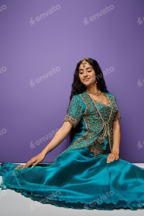 Preview: vertical shot of attractive indian woman sitting on floor in blue traditional sari and looking away