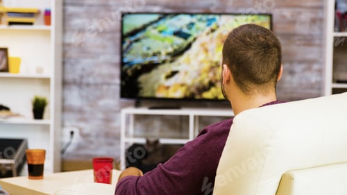 Preview: Back view of young man sitting on chair eating popcorn
