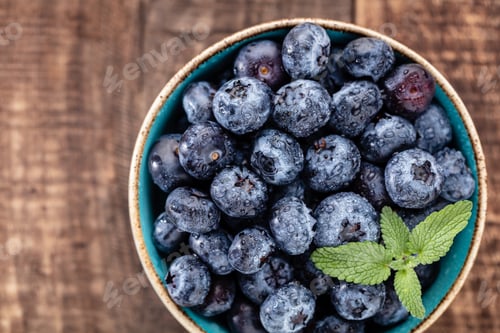 Preview: Ripe blueberries with water drops in a bowl on a wooden background,