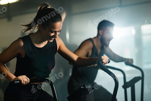 Preview: Happy athletic woman having sports training on exercise bike in a gym.