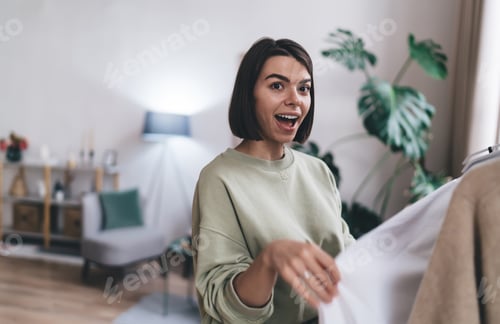 Preview: Amazed female choosing clothes from rack at home