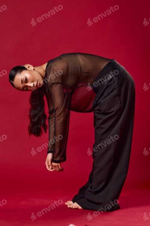 Preview: Asian woman in black pants and sheer top picking up a tennis ball against a red background