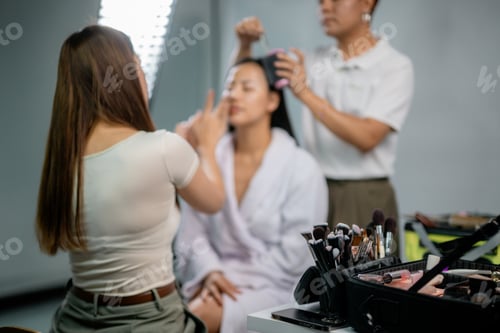 Preview: Makeup artist applying cosmetics on model's face in professional studio