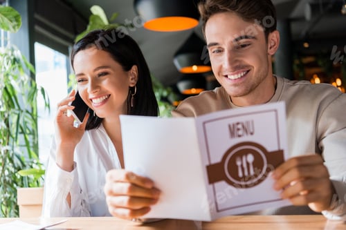 Preview: selective focus of happy man holding menu near woman talking on smartphone