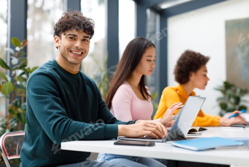 Preview: Cheerful latin male student with classmates using laptops