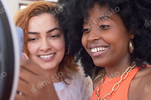 Preview: two young girls of different ethnicities smiling and checking a telephone