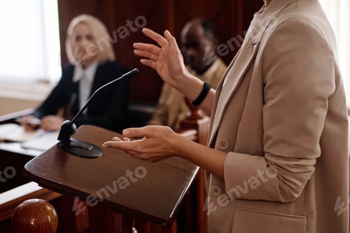 Preview: Cropped shot of young female witness in beige blazer standing by tribune