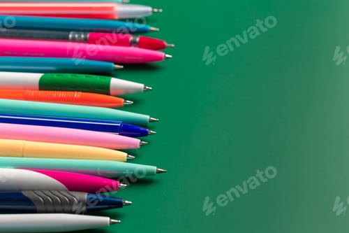 Preview: Colorful pens arranged in a straight line on a green surface during daytime