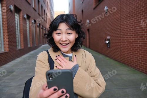 Preview: Portrait of amazed girl, looks at smartphone screen and gasps from happiness, reads good news on