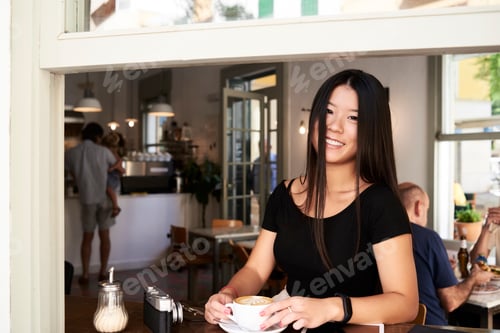 Preview: Happy asian woman in a coffee shop next to the window