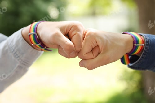 Preview: LGBT concept. Women in rainbow wristbands holding fists together outdoors, closeup