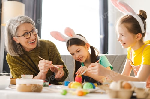 Preview: Grandmother and granddaughters painting easter eggs together at home