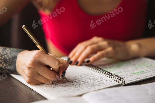 Preview: Close-up woman's hand holding a pencil and writing information in a notebook