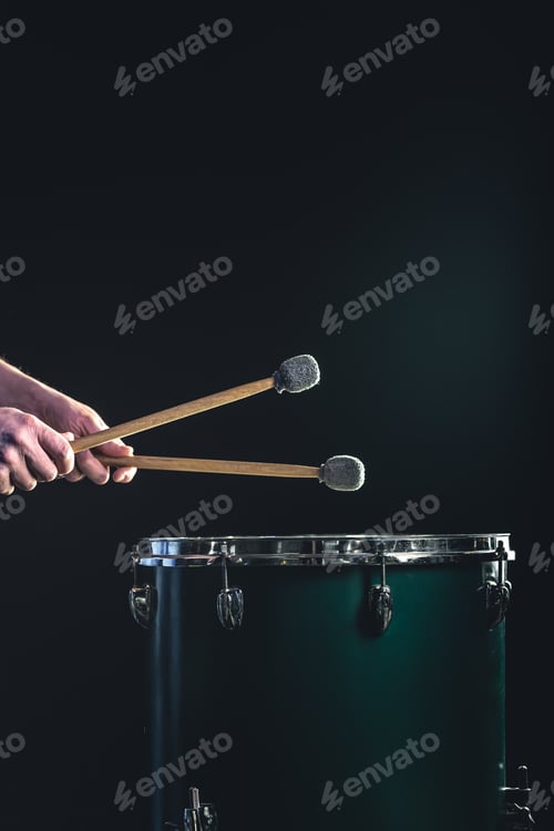 Preview: A man plays a musical percussion instrument with sticks on a dark background.
