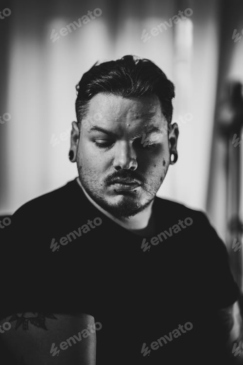 Preview: Grayscale vertical shot of a Caucasian sad man with earing looking down