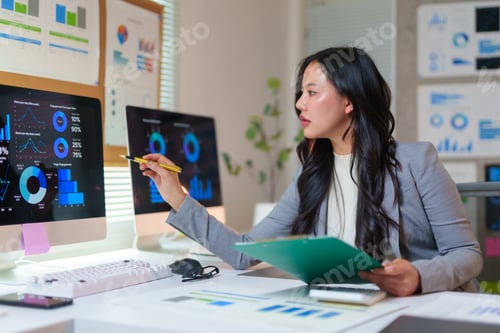 Preview: Asian businesswoman pointing at computer screen analyzing financial charts and graphs