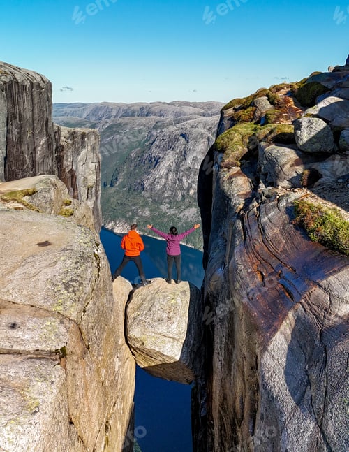 Preview: Adventurers Standing onKjeragbolten Edge Overlooking Norways Majestic Fjords
