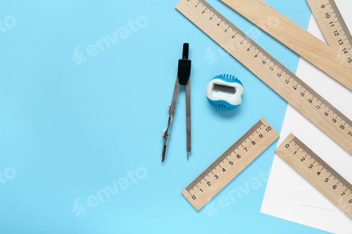 Preview: Different rulers, pencil sharpener and compass on light blue background, flat lay. Space for text