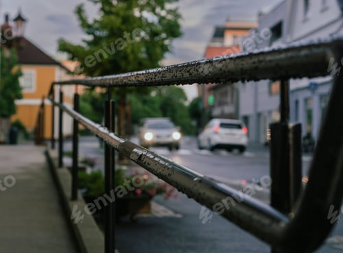 Preview: Wet metal railing alongside a road with cars passing in the town of Rakkestad, Norway