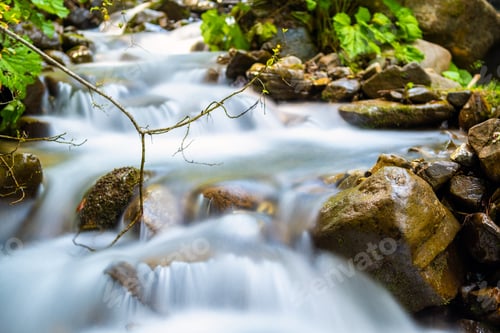 Preview: Mountain river with small waterfall with clear turquoise water falling down between wet boulders