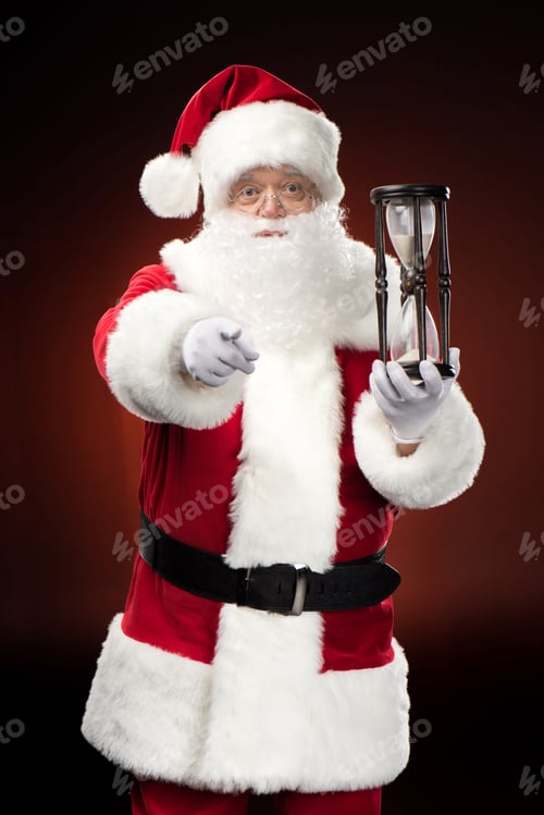 Preview: Santa Claus with hourglass and pointing at camera