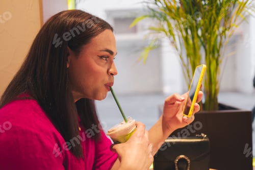 Preview: Trans woman drinking matcha tea and using cellphone. LGBT concept.
