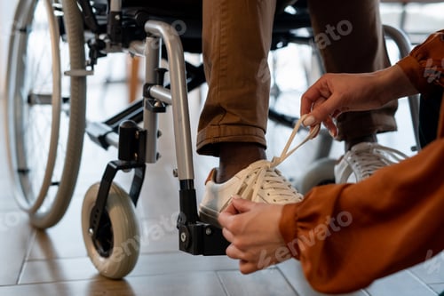 Vorschau: Hände einer jungen Pflegerin beim Binden von Schnürsenkeln an Schuhen eines behinderten Mannes