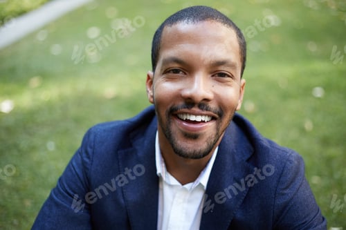 Preview: Portrait of happy confident young African-American businessman in formal wear sitting at city park.