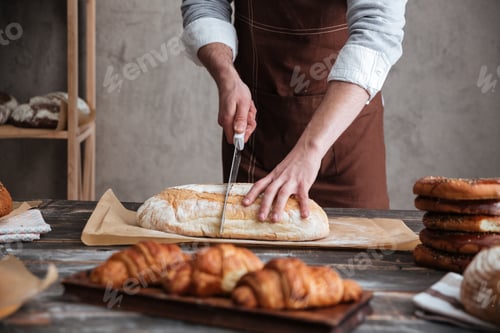 Preview: Cropped image of young man baker cut the bread.