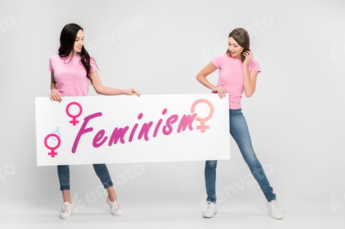 Preview: cheerful women holding large sign with feminism lettering on grey background