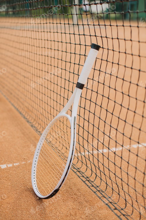 Preview: Tennis racket leaning against net on clay court