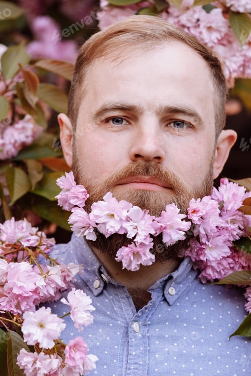 Preview: brutal bearded man in the flowering cherry trees. Handsome smiling bearded man outdoors. Spring day