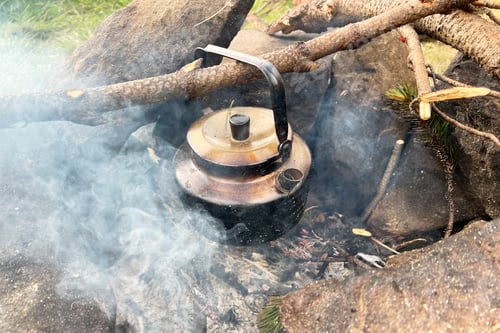 Preview: Blackened kettle heating over campfire. Smoke swirls around kettle, and hint of green pine needles.