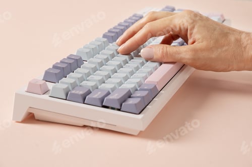 Preview: Womans hand typing on keyboard on pink background.