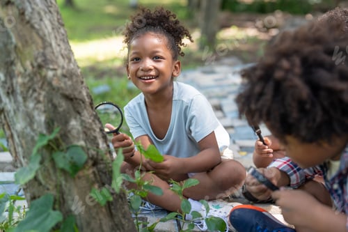 Preview: Smiling african american little girl with friends hold magnifying glass to explore on tree in park