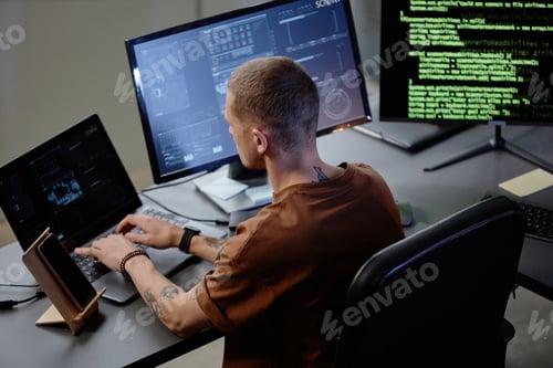 Preview: Male IT Programmer Using Laptop at Workstation with Several Computers in Office