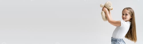 Preview: smiling girl holding teddy bear and looking at camera isolated on grey, banner