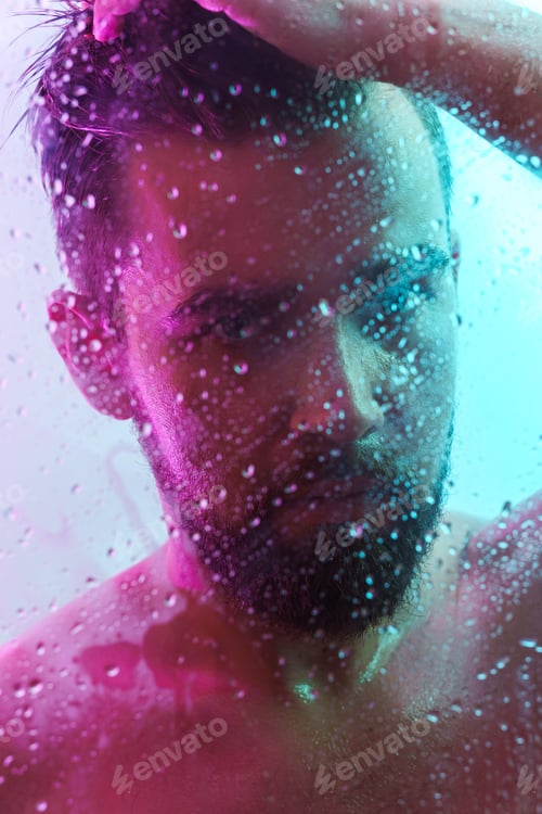 Preview: Portrait of handsome young man captured through wet glass in colorful light
