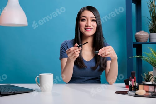 Preview: Asian creator woman filming makeup tutorial using black mascara