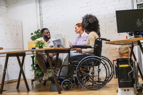 Preview: Diverse businesspeople collaborating in modern coworking space, two in wheelchairs