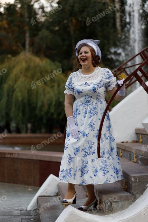 Preview: A woman in vintage clothes and a hat stands against the background of a fountain in an autumn park