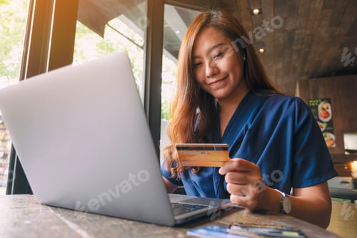 Preview: A beautiful asian woman holding credit cards while using laptop computer