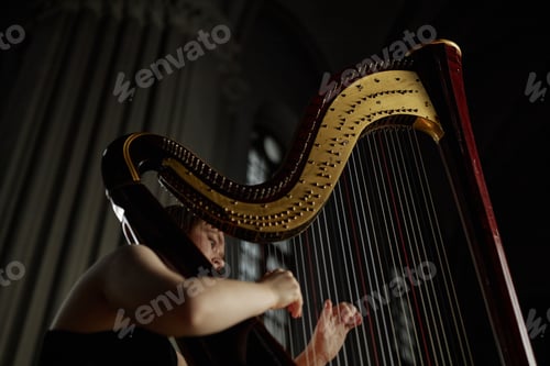 Preview: Female Musician Playing Music on Antique Wooden Harp in Dim Light Indoors