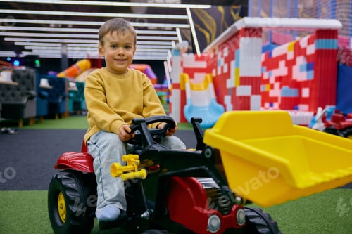 Preview: Little boy preschooler riding toy tractor at indoor playground