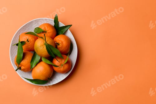 Preview: Fresh cutted clementines and whole mandarin over round plate on colored background